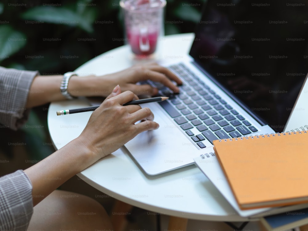 Foto cortada de mãos femininas trabalhando com laptop na mesa de café com caderno e papelada no café