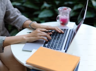 Vue latérale des mains féminines travaillant avec un ordinateur portable sur une table basse avec un cahier et de la paperasse dans un café