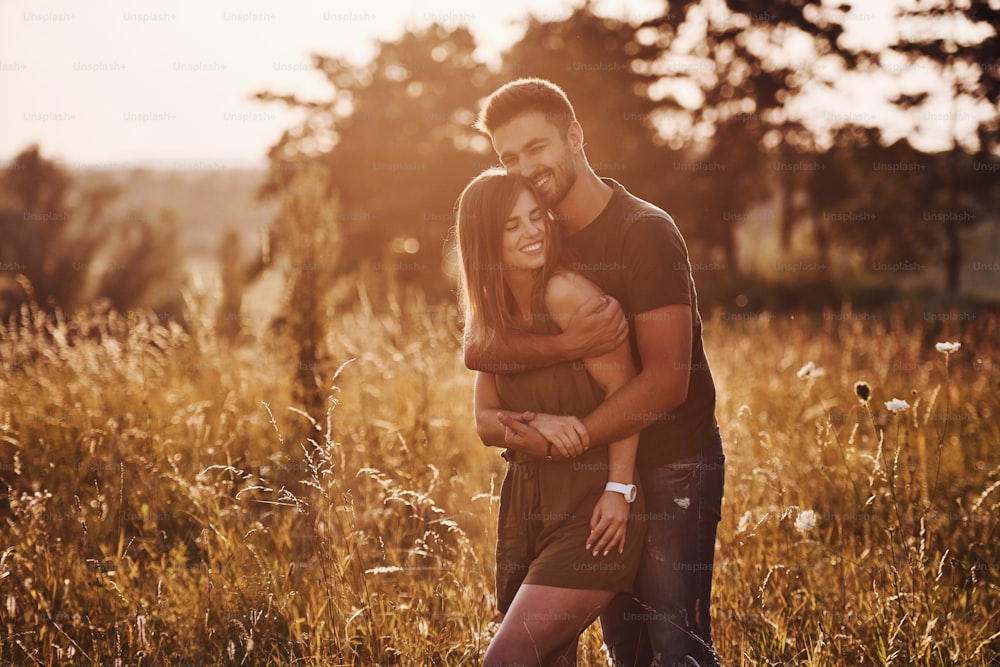 In the field illuminated by the sunlight. Beautiful young couple have a good time in the forest at daytime.