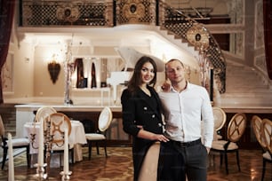 Stands against stage with piano. Beautiful couple have romantic dinner in luxury restaurant at evening time.