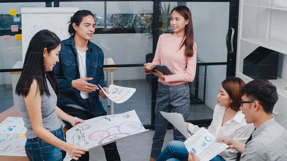 Glückliche junge asiatische Geschäftsleute und Geschäftsfrauen treffen sich mit Brainstorming-Ideen über neue Papiere Projektkollegen, die zusammenarbeiten und die Erfolgsstrategie planen, genießen Teamarbeit in einem kleinen, modernen Büro.