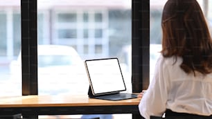 モダンなカフェに座りながらタブレットコンピュータで作業する若い女性起業家の後ろ姿。
