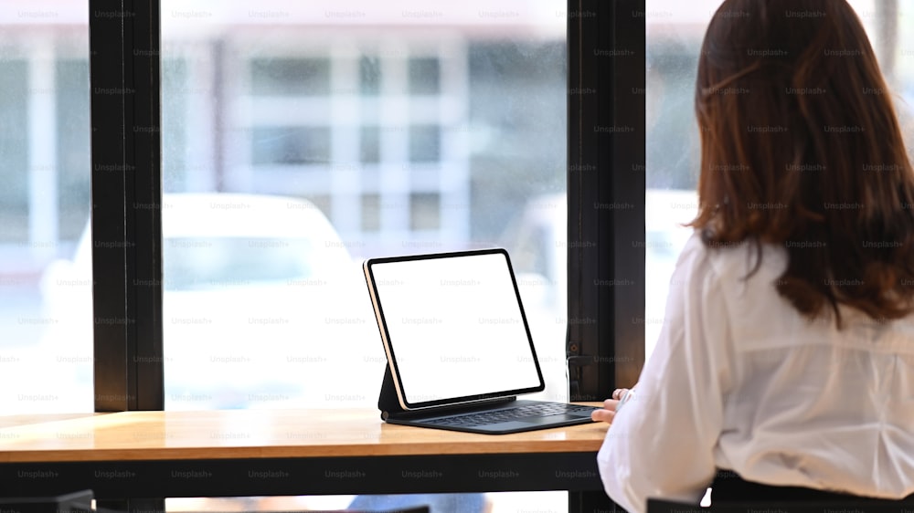 Vista posteriore della giovane imprenditrice che lavora con il tablet mentre è seduta in un moderno caffè.