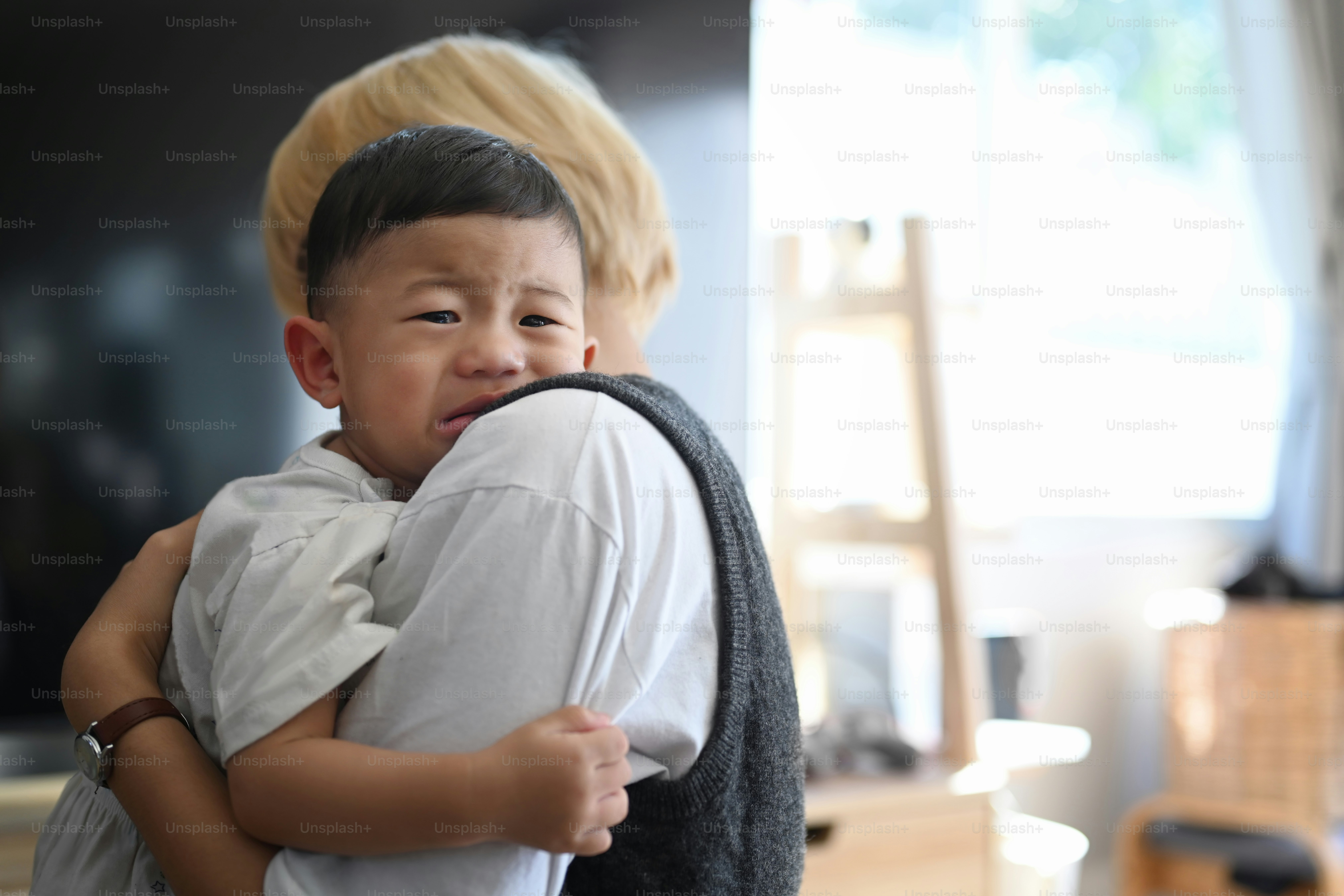 Mother caressing and calming down her crying baby son while standing in living room.
