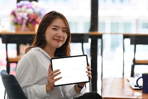 Confident businesswoman showing digital tablet while sitting in office. Blank screen for your advertising text message or promotional content.