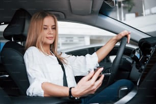 It's new message. Beautiful blonde girl sitting in the new car with modern black interior.