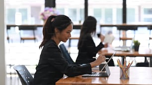 Cheerful businesswoman working on her project on tablet computer while sitting with her colleague in modern office.