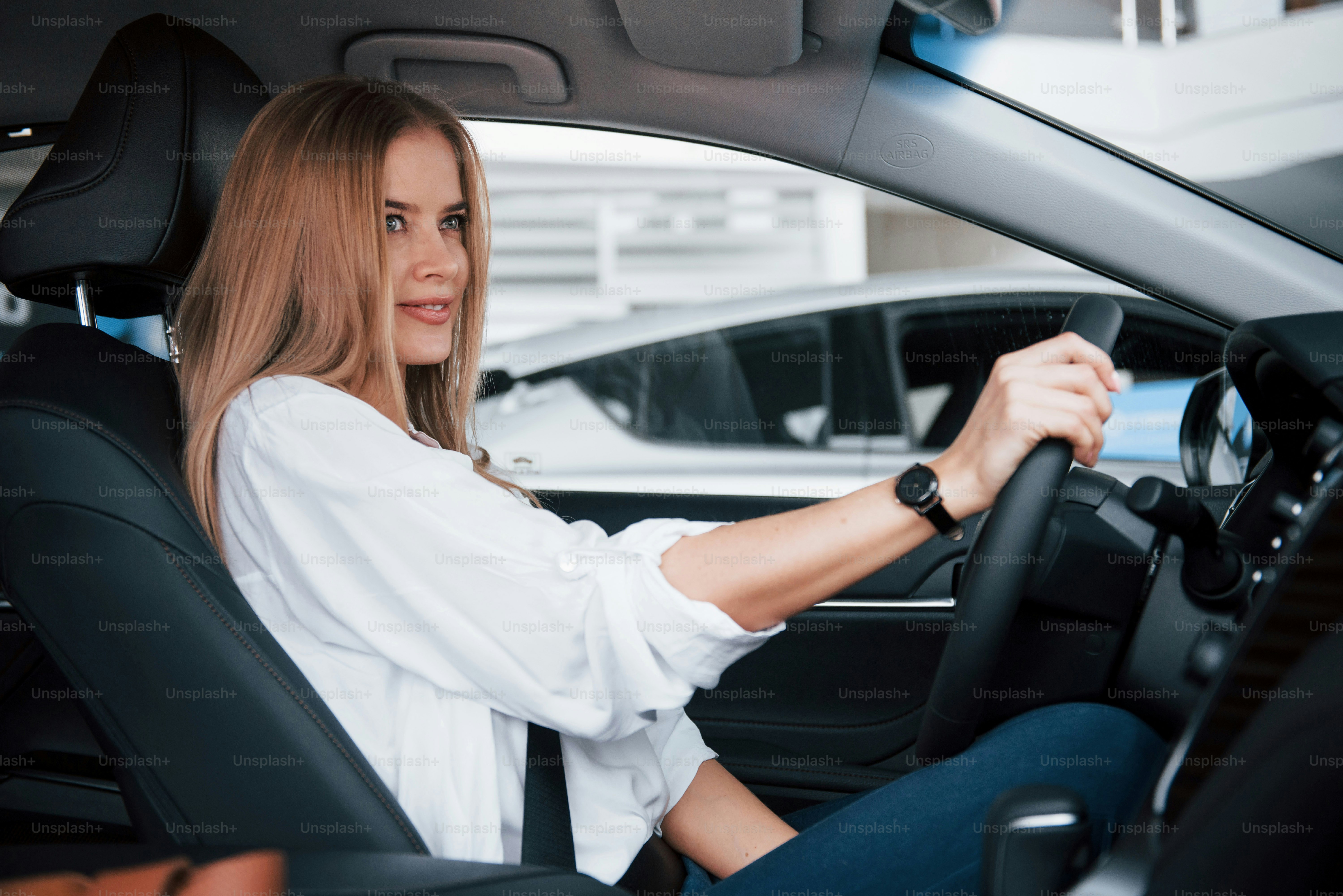 Mira frente a ella. Hermosa chica rubia sentada en el coche nuevo con interior negro moderno.