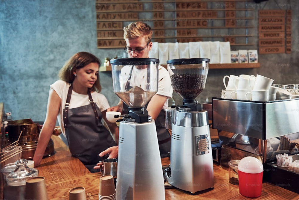 Behind the coffee machine. Two young workers indoors. Conception of business and service.