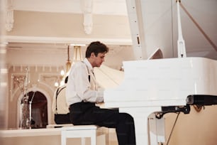 Junger Berufsmusiker in offizieller Kleidung spielt auf dem weißen Klavier.