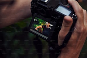 Las manos del fotógrafo sostienen la cámara. Backstage de la sesión de fotos en el bosque. Hombre de camisa negra.