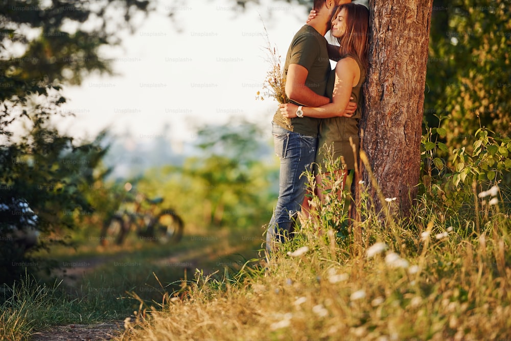 Leaning on the tree. Beautiful young couple have a good time in the forest at daytime.