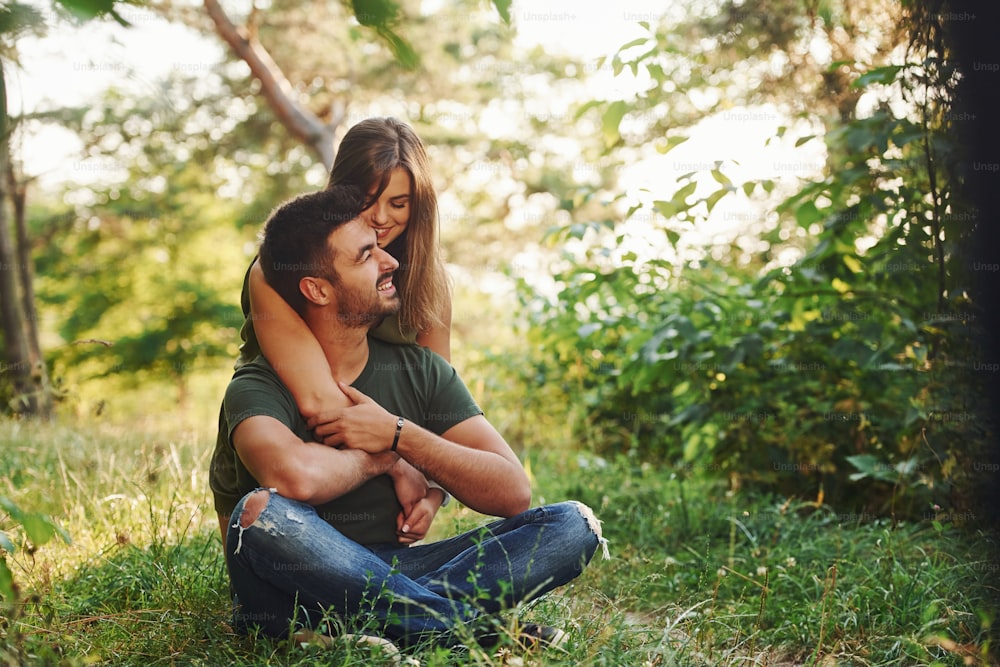座って抱きしめる。美しい若いカップルは、昼間の森で楽しい時間を過ごしています。