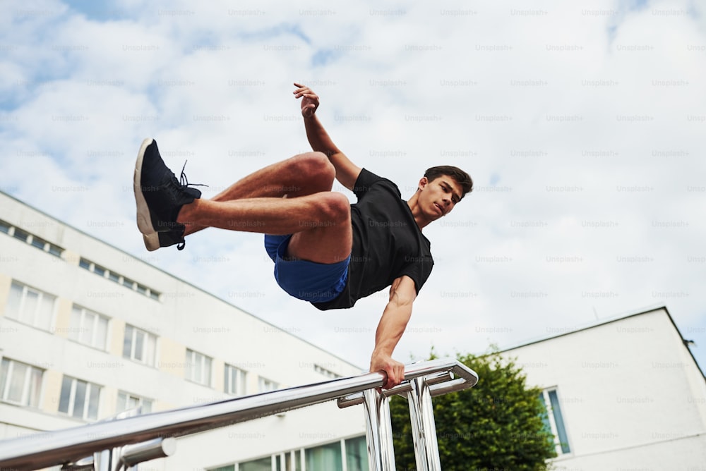 Silver colored railings. Young sports man doing parkour in the city at sunny daytime.