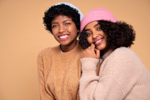 Cheerful, positive, smiling afro female friends posing together, wearing colorful hipster cap, looking at camera.