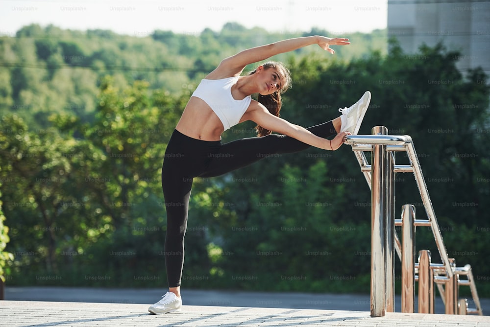 Sportive woman doing fitness exercises in the city at daytime. Near the railings.