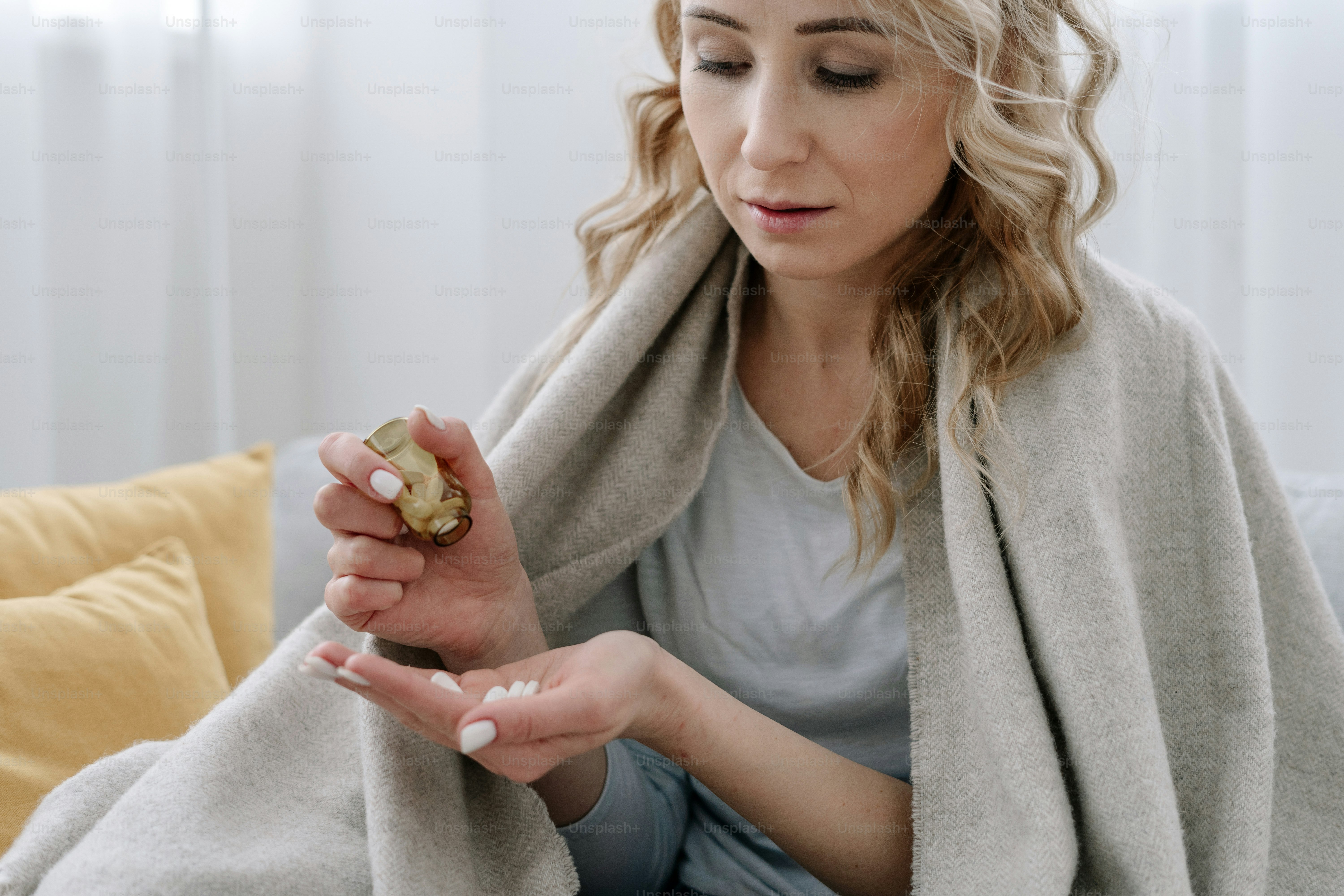 Vitamin, multivitamin and supplements concept. Ill and calm woman covered with plaid, sit on sofa at home, holding bottle with small pills in hand, looking at medicine before taking inside