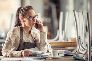 Restaurant owner consults bookeeping with her accountant sitting over paperwork with a coffee.