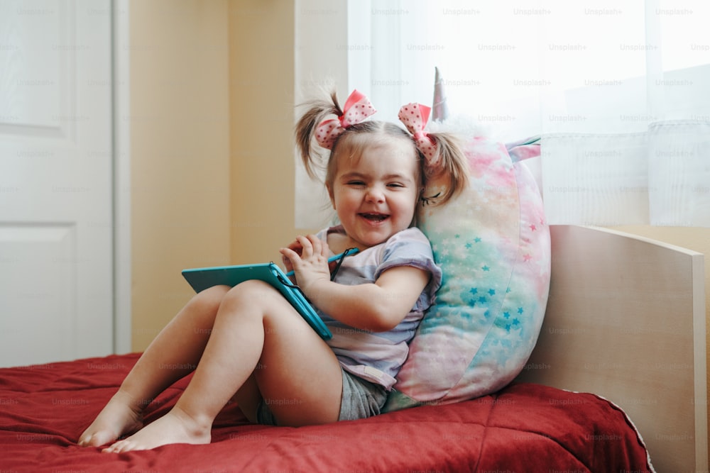 Lustiges süßes lächelndes Kleinkind-Baby-Mädchen, das mit Stift auf digitalem Zeichenblock-Tablet zeichnet. Kleines Kind, das Technologie benutzt. Entwicklung der frühkindlichen Bildung. Glückliche authentische häusliche Lifestyle-Kindheit.