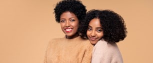 Two young beautiful afro women posing together, hugging and smiling to the camera. Real people emotions.