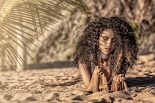 Sensual woman with afro hairstyle relaxing on the sandy beach.