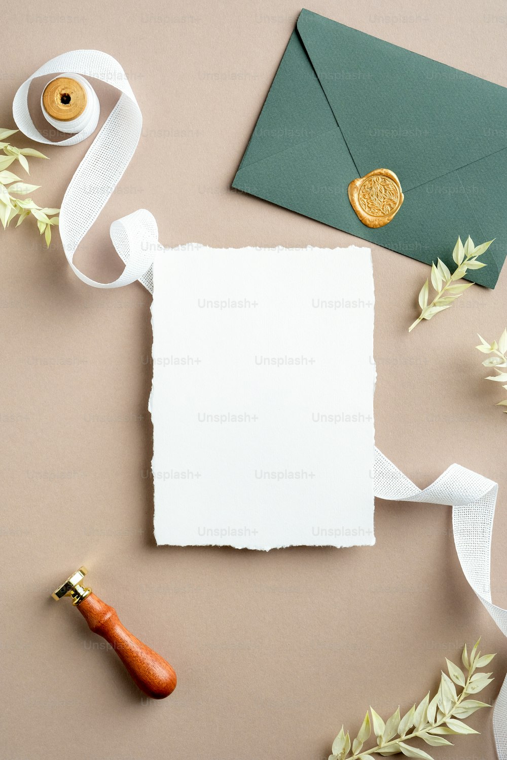 Ripped sheet of paper, silk ribbon, green envelope with wax seal, dried flowers on pastel beige background. Wedding invitation card template. Flat lay, top view, copy space.