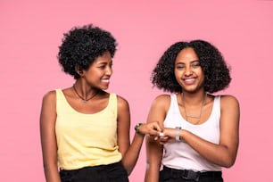 Young beautiful and happy afro female friends smiling to the camera, having fun together. Girls posing on the pink pastel studio background.