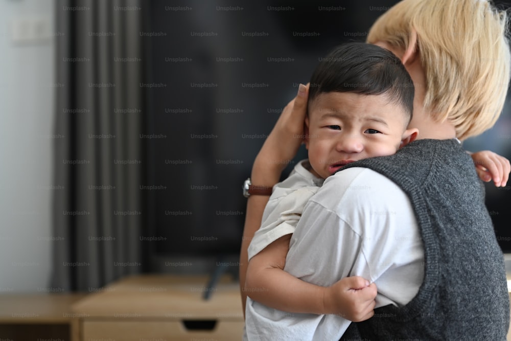 Imagen de una madre asiática sosteniendo a un bebé llorando en una casa cómoda.