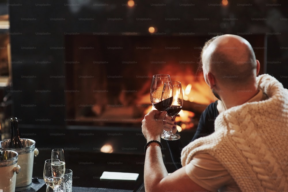 Bald guy with glass of champagne feels satisfaction sitting near the fireplace in the restaurant.