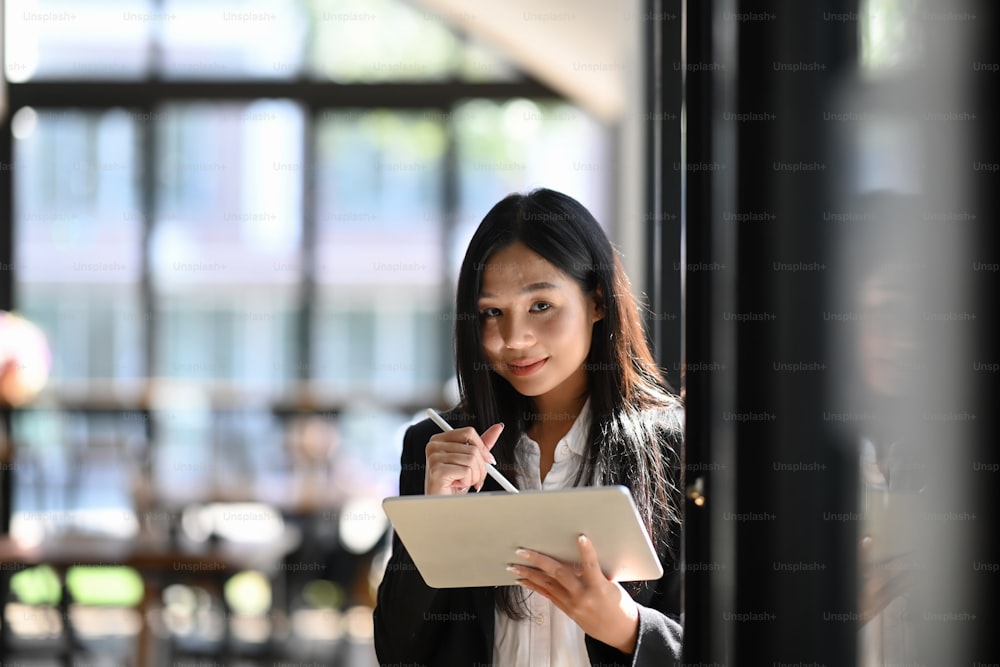 Geschäftsfrau mit digitalem Tablet und Eingabestift, während sie in der Nähe des Fensters im Büro steht.