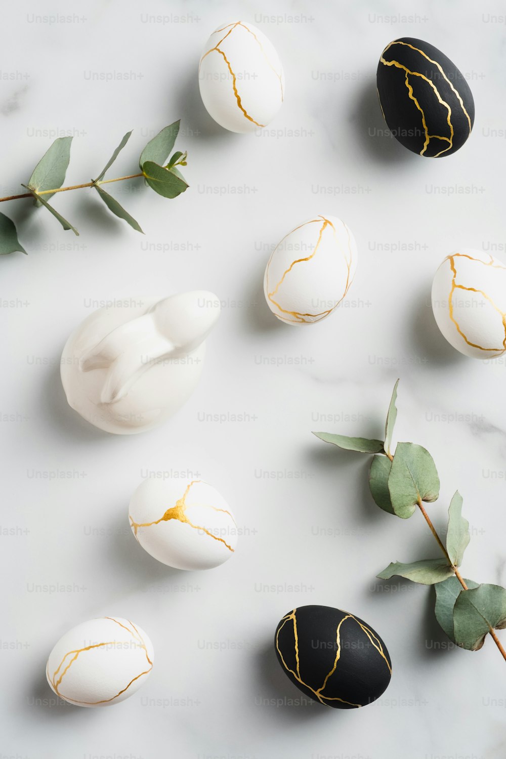 Easter flat lay composition with luxury easter eggs, bunny rabbit, eucalyptus leaves on marble background.