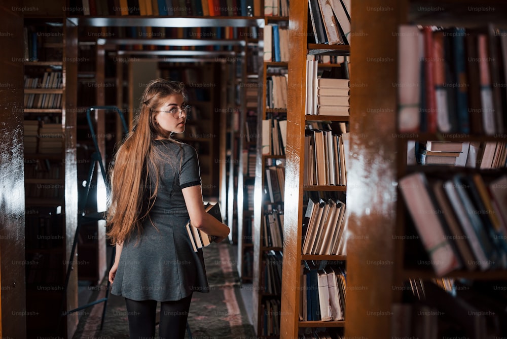 뒤를 본다. 여학생은 책으로 가득 찬 도서관에 있습니다. 교육의 개념.