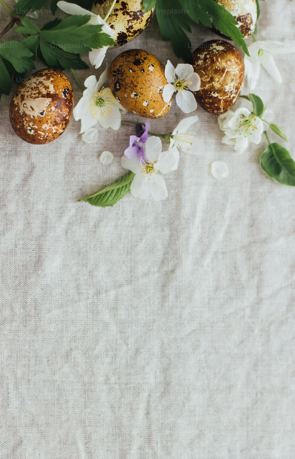 Easter eggs with spring flowers on rustic linen background, flat lay with space for text. Stylish modern easter and quail eggs with natural dye and spring blooms. Aesthetic seasons greeting card