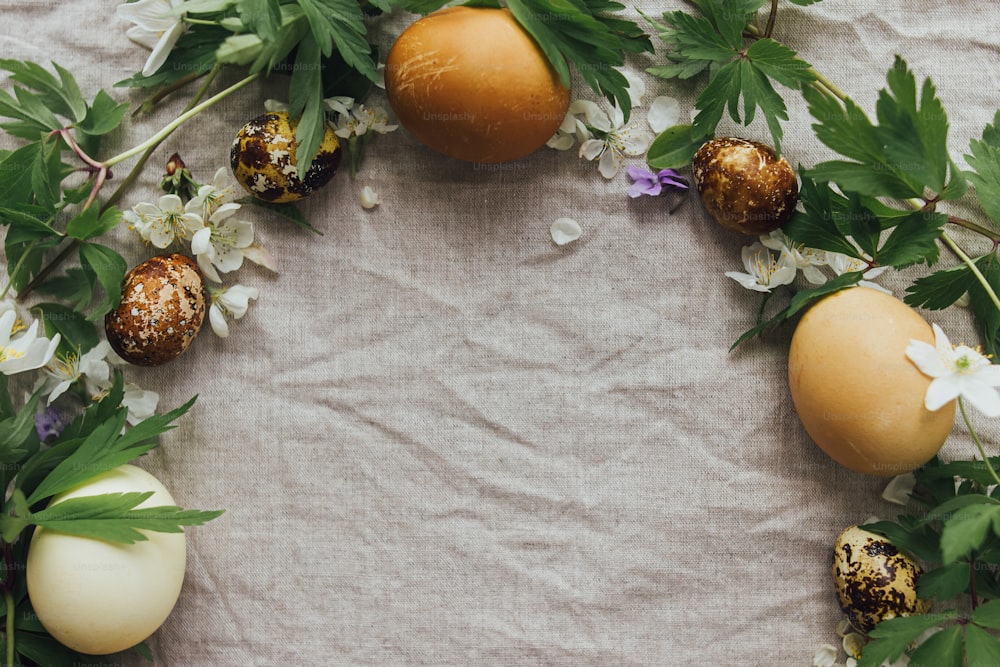 Ostereier und Frühlingsblumen im Rahmen auf rustikalem Leinenhintergrund, flach gelegt mit Platz für Text. Stilvolle Ostereier in Naturfarbe und Blüten, ästhetische Weihnachtsgrüße