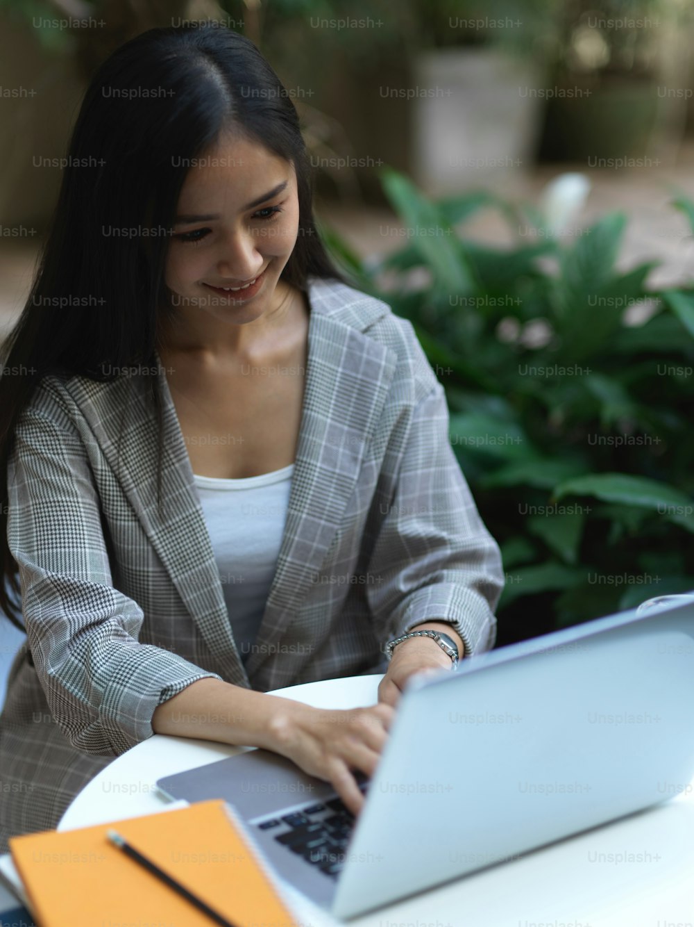 Porträt einer Geschäftsfrau, die am Laptop auf dem Couchtisch mit Notizbüchern im Café arbeitet