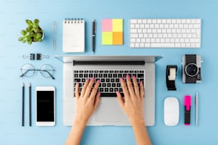 Toma aérea de las manos de la mujer usando una computadora portátil sobre una mesa azul. Escritorio de oficina con accesorios. Tendido plano