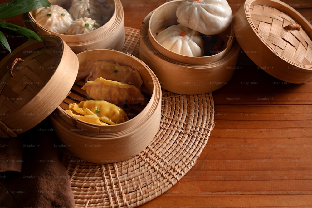 Cropped shot of bamboo steamers with dumplings and pork bun on wooded table in kitchen