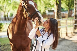 Dare un bacio. Veterinario femmina che esamina il cavallo all'aperto presso la fattoria durante il giorno.