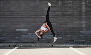 Doing crazy parkour and athletic stunts. Young sportive brunette with slim body shape against brick wall in the city at daytime.