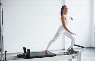 Chica concentrada. Mujer deportiva joven segura de sí misma con un tipo de cuerpo delgado en el centro saludable que hace ejercicios mediante el uso de equipos especiales.