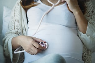Cropped shot of Asian pregnant woman using stethoscope the doctor listening to the sound of the baby in the stomach.