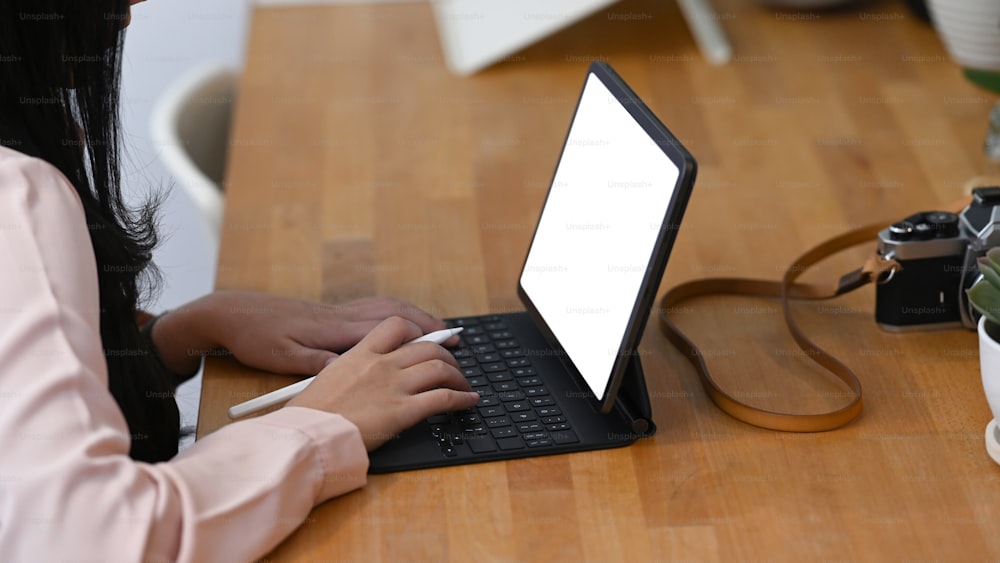 Seitenansicht einer jungen Fotografin, die mit einem Tablet-Computer auf einem Holztisch arbeitet.