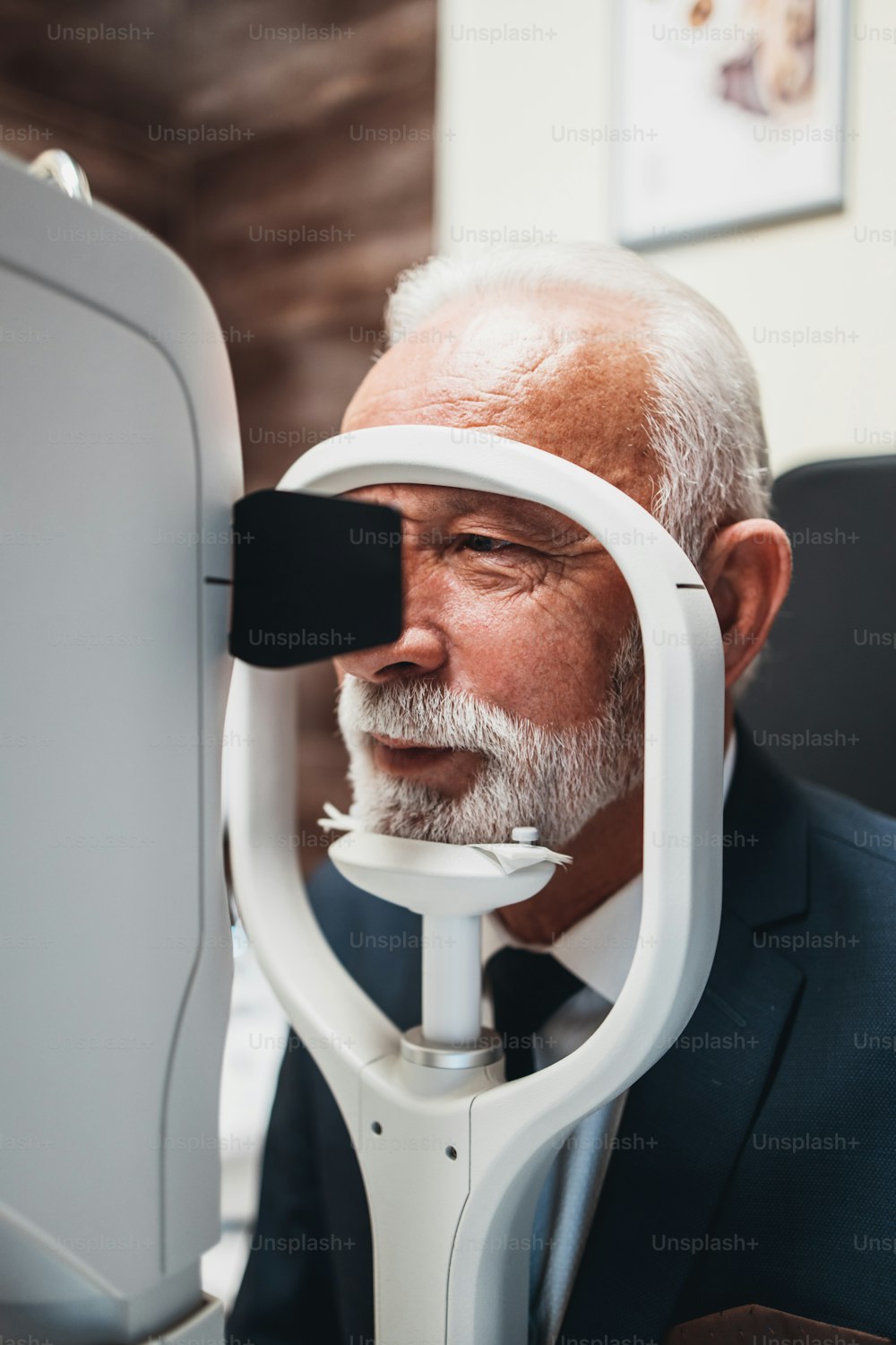 Elegant senior bearded man receiving ophthalmology treatment. Doctor ophthalmologist checking his eyesight with modern equipment.