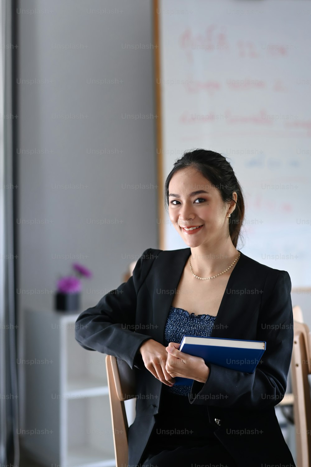 Portrait of cheerful businesswoman holding book and sitting in modern office.