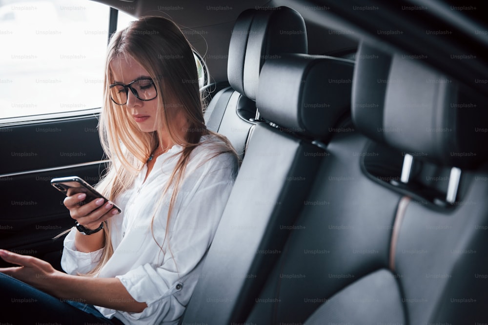 Algún tipo de información interesante. Una mujer de negocios inteligente se sienta en el asiento trasero del automóvil de lujo con interior negro.