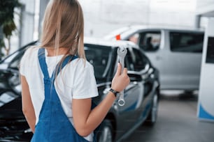 Standing in front of vehicles. Nice blonde woman repairer is on her work. Indoors at car shop.