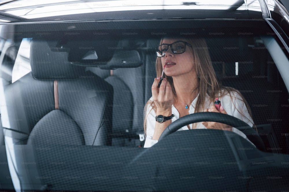 Prestigiosa empresaria. Hermosa chica rubia sentada en el coche nuevo con interior negro moderno.