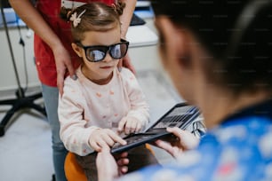 Beautiful and adorable little girl receiving ophthalmology treatment. Doctor ophthalmologist checking her eyesight with modern equipment.