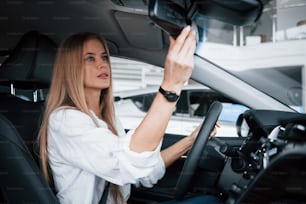 Tourner le miroir. Belle fille blonde assise dans la nouvelle voiture avec un intérieur noir moderne.