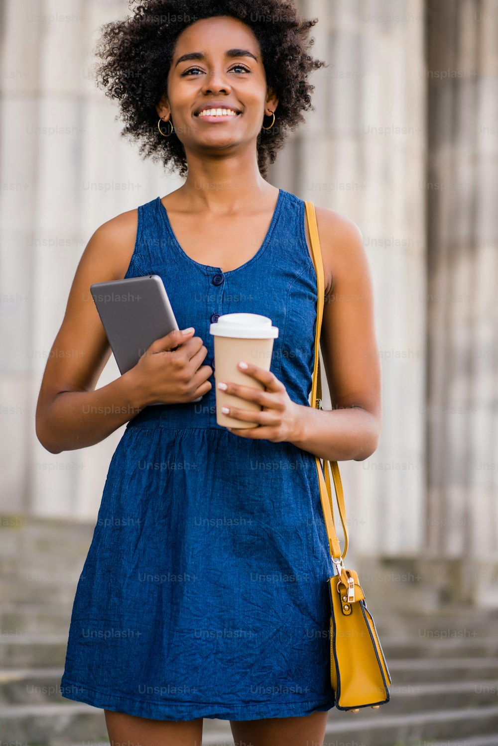 Retrato de una mujer de negocios afro sosteniendo una tableta digital y una taza de café mientras está de pie al aire libre en la calle. Concepto empresarial y urbano.
